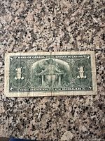 Back side of the 1937 Canadian one dollar bill, showing the intricate green ornamental design and denomination text.