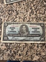 Front of the 1937 Canadian $5 banknote showing portrait of King George VI with bilingual 'Bank of Canada' text and serial numbers.