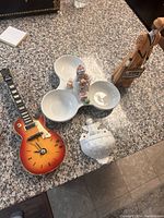 Photo of the ceramic Les Paul style guitar clock, ceramic three-section dish, Santa Claus figurine, white decorative container, and tall figurine with chalkboard