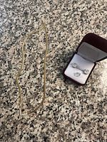 Full view of the gold-tone snake chain necklace and jewelry box containing the earrings and single stud on a granite countertop.