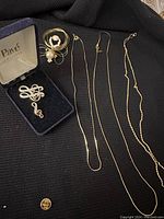 Overview of all jewelry items laid on black fabric showing musical note pins, chain necklaces, and wire brooch with pearls.