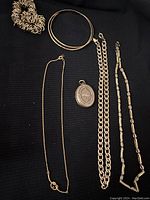 Photo showing assorted gold tone jewelry pieces and one fabric scrunchie laid on black background.