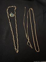 Three gold-tone necklaces and one pendant laid on black fabric background, showing link styles and pendant design.