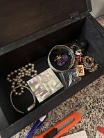Open black carved wooden jewelry box with assorted jewelry inside on granite countertop