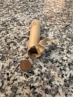 Paper brown penny roll partially torn with pennies next to it on granite surface