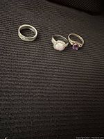 Photo showing three rings: silver band, opal with clear stones ring, and amethyst-like stone ring