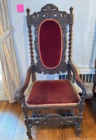 Full front view of carved wooden armchair with velvet seat and back