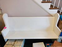 Front view of white wooden pew bench showing scratches and wear on the seat and backrest.