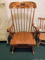 Front view of antique rocking chair showing curved top rail with painted floral and basket design, spindle backrest, and wooden seat.