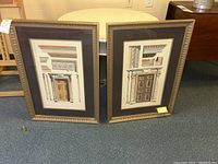 Two framed architectural prints standing side by side on floor showing ornamental doorways with gold-tone frames and black matting.
