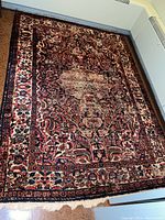 Full view of the rectangular area rug with dark floral pattern and visible wear in the center, placed on floor against walls.