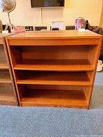 Front view of one wooden bookcase showing three open shelves and scratches on surfaces.