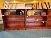 Front view of two matching wooden bookcases with boxed books and decorative items on shelves and tops.
