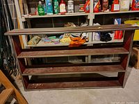 Front view of the wood bookshelf showing three shelves and visible wear, placed in a storage area with cleaning supplies in background.
