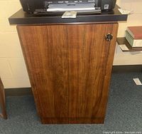 Front view of wooden cabinet with wood grain finish, black top, lock on door