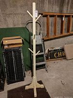 Full view of the wooden coat tree next to a ladder and other items in a storage area.