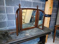 Full view of freestanding triple fold mirror on metal table against a concrete block wall, showing the mirror with side panels partially open.