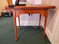 Side view of wooden hinged leaf side table showing leg details and surface wear.