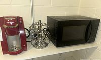 Keurig coffee maker, black microwave, and metal K-Cup holder on shelf