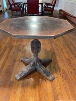 Front view of vintage octagonal wooden table showing the carved pedestal base and four legs on hardwood floor.
