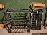 Two completed Rubbermaid black plastic shelving units with three vertical shelves each, situated near unassembled shelving parts stacked upright.