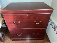 Front view of two-drawer Sauder Woodworking file cabinet with brass handles and lock keyhole.