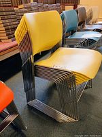 Side view of stack of ten yellow chairs showing tubular metal frame and molded yellow seat/back design