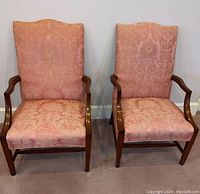 Front view of two matching upholstered arm chairs with pink damask fabric and wooden arms and legs.
