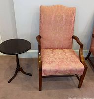 View of upholstered armchair with wooden arms next to round wooden side table