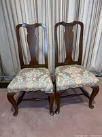 Pair of dark wood chairs with floral upholstered seats, showing full front view.