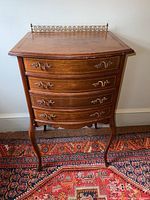 Front view of vintage wooden cabinet showing four dovetail drawers with brass handles, curved legs, and brass rail on top.