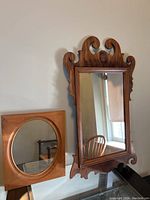 Two vintage wooden framed mirrors displayed together, one with decorative carved top and one with circular inset mirror.