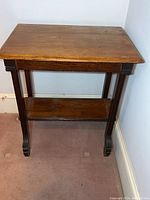 Front view of the dark wooden side table showing the top surface, four legs, and lower shelf against a light wall.
