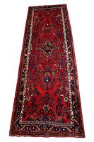 Full view of the Hamadan runner rug showing red background with minimal floral and geometric designs. Visible borders with mixed cream, brown, and blue colors. Rug shows signs of wear.
