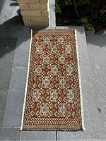Full view of Persian rug backrest lying flat outdoors showing repeating geometric pattern and fringe ends