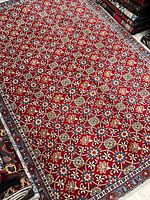 Full view of red floral Persian rug displayed on store floor