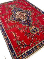 Persian Tabriz handmade rug with red background and ornate central medallion, floral accents, and blue border with geometric details.