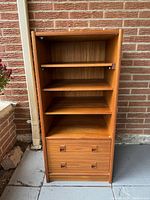 Front view of mid century media cabinet showing three open shelves and two drawers at bottom.