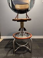 Front view of Western Electric telephone operator's chair showing wooden cane seat, circular footrest, metal legs, padded backrest and swivel/height adjustment mechanism.