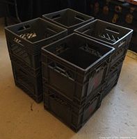 Stack of 8 grey plastic milk crates showing top and side views with ventilation holes and molded handles.