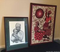 Photo showing both framed art pieces side by side against a beige wall: left piece is the graphite drawing of woman and child, right is fabric artwork on wood frame.