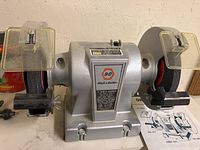 Front view of Black & Decker 5 inch bench grinder showing dual grinding wheels with eye shields, wheel guards, tool rests and main body with label.