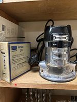 Craftsman router next to the Sears Craftsman Attach Lite box for a battery-powered light on a wooden shelf.