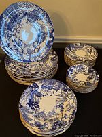 Full view of stacked dinner, dessert, bread/butter and fruit plates on black surface showing blue chinoiserie pattern and gold rims