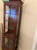 Front and side view of two-tiered dark wood curio cabinet with glass doors and lighting.