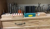 Overall view of drill bits, transfer punch set, and Allen keys organized on wooden stands and holders