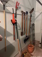 Full view of garage lot showing leaf rakes, hedge trimmer, spades, flower pots, and trellises