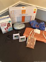 Full view of all items on black surface including heating pads, white noise machine, thermostats and warming bag