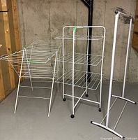 Three white metal laundry drying racks arranged together in a basement space, visible against a concrete wall.