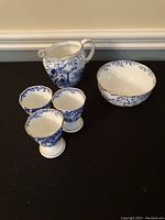 Creamer, sugar bowl, and three egg cups arranged on surface showing pattern, color, and sizes